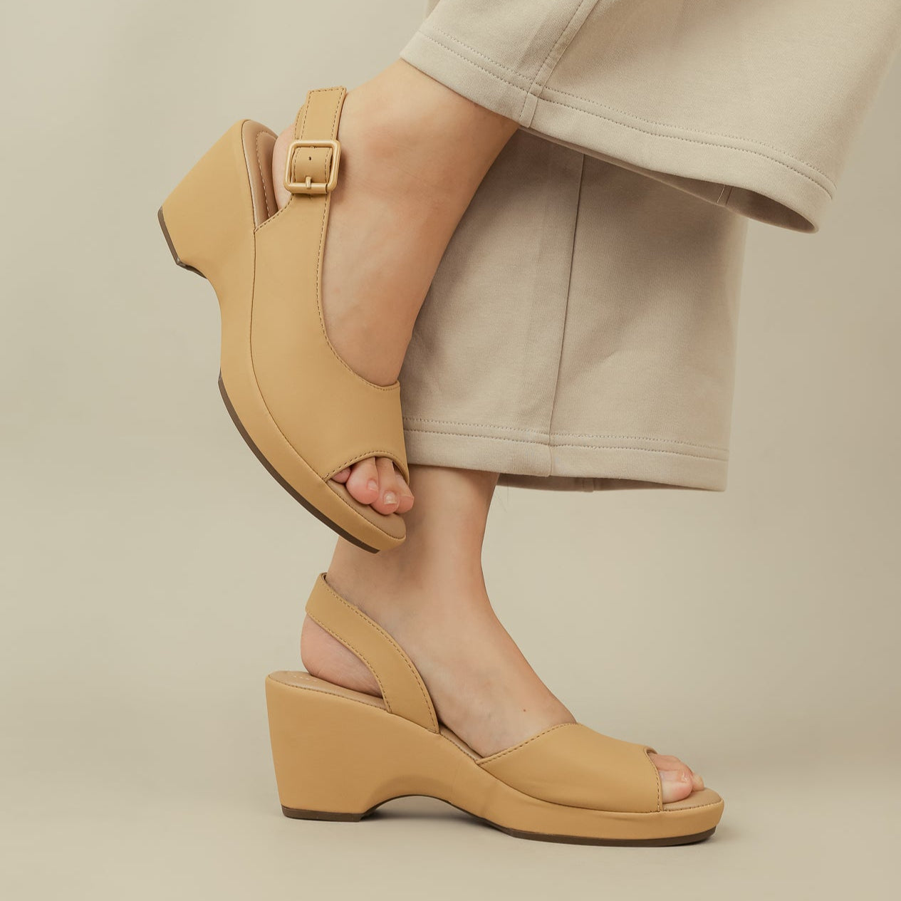 Tan sandals worn with beige pants on a neutral background
